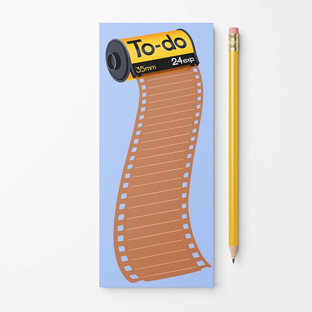 A rectangular notepad with a light blue background and a cartoon film roll graphic reading 'To-do 35mm 24exp' in orange, black, and yellow, shown next to a yellow pencil on a white background.