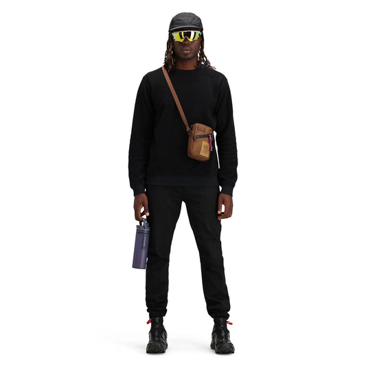 Person wearing a black outfit with a brown crossbody bag on a white background