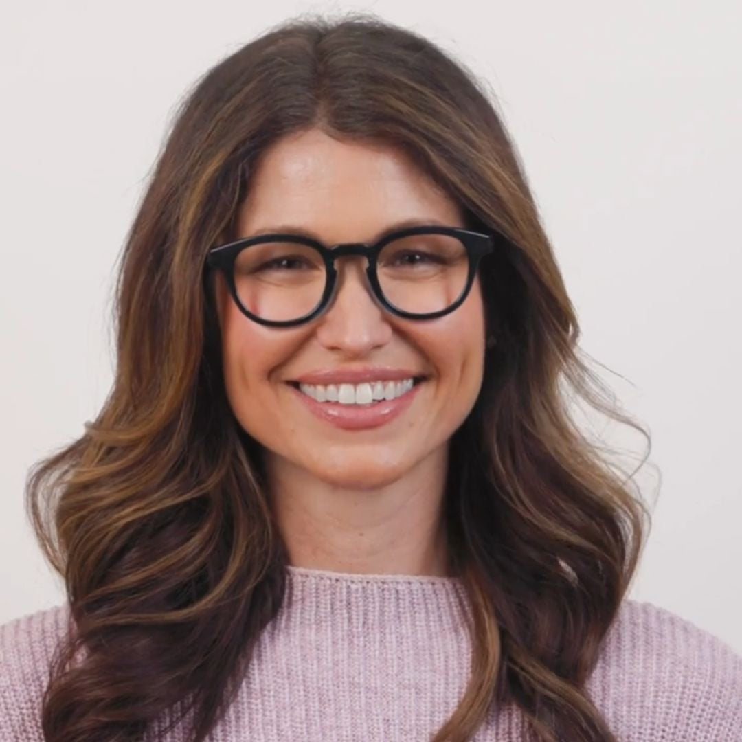 Woman wearing teal glasses and a light pink sweater against a plain background