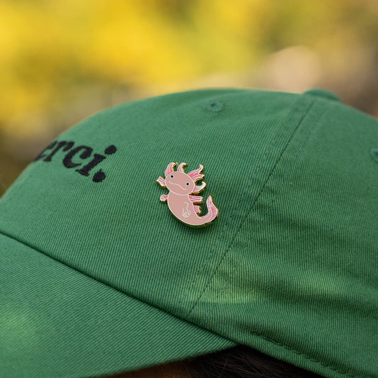 Green cap with a pink axolotl pin against a blurred natural background