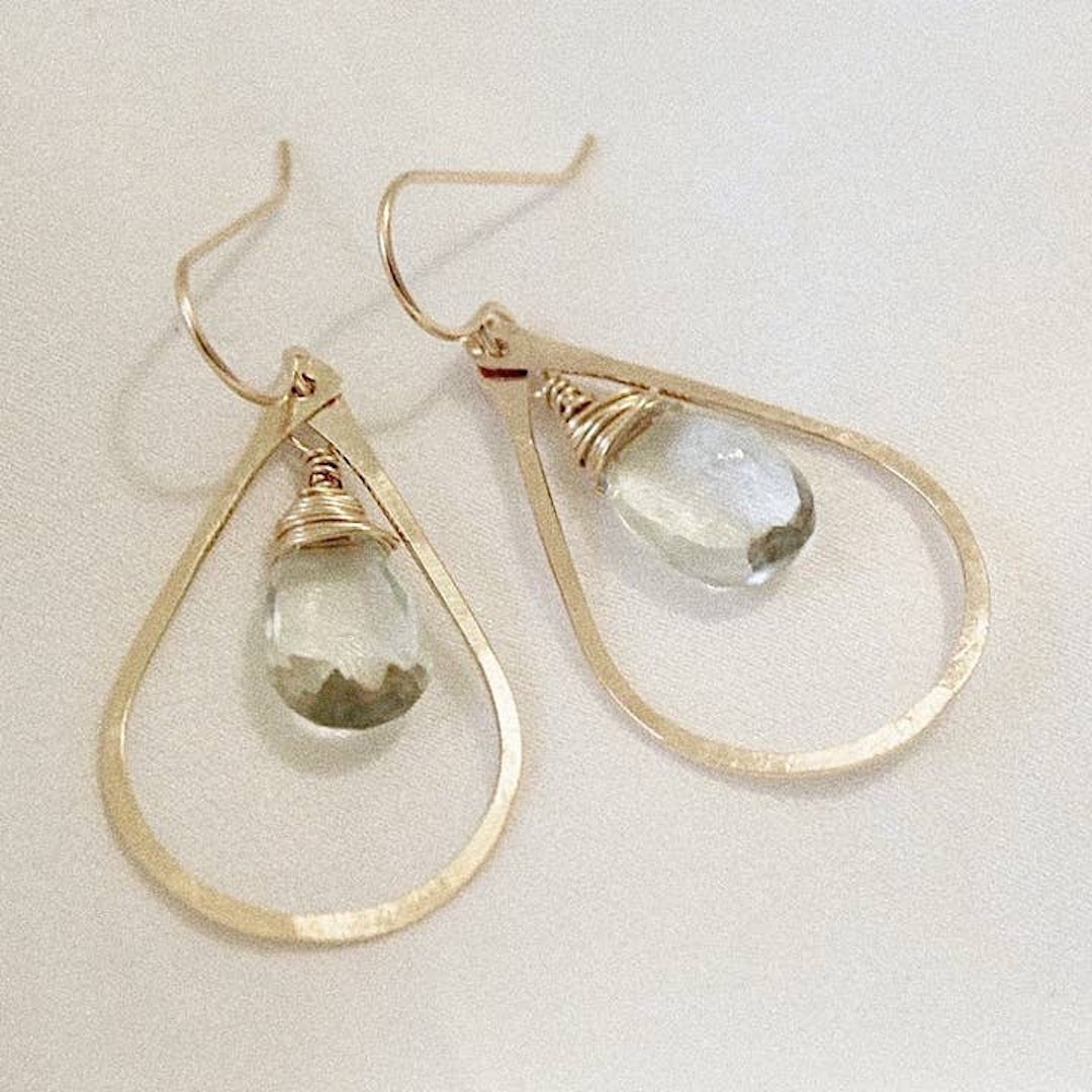 Gold hoop earrings with teardrop-shaped sage green gemstones on a light background