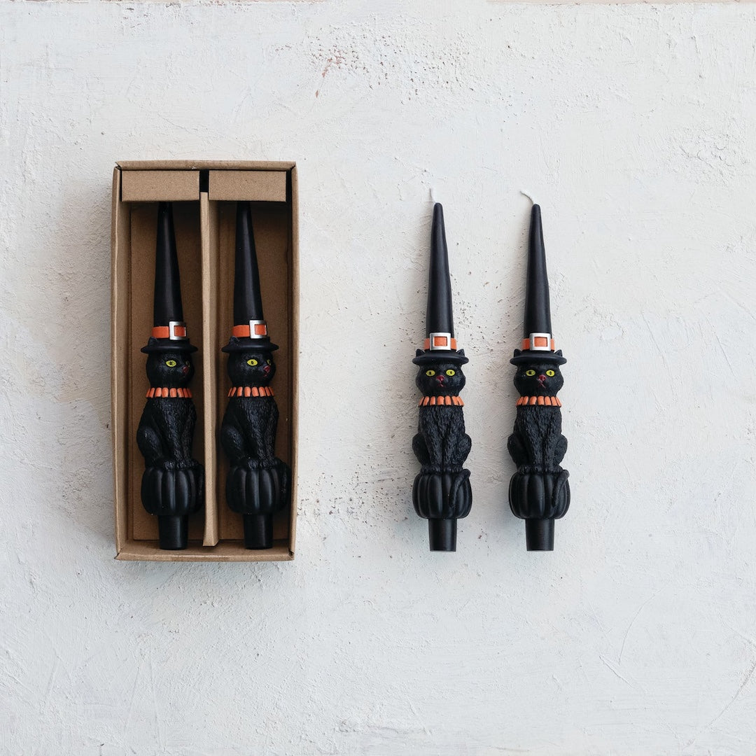 Black cat-shaped candles with witch hats on a white background