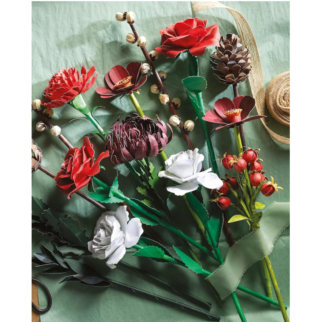 A collection of artificial paper flowers and buds arranged on a textured sage green background, featuring red, white, and dark burgundy blossoms with green leaves and stems, alongside a brown twine ribbon.