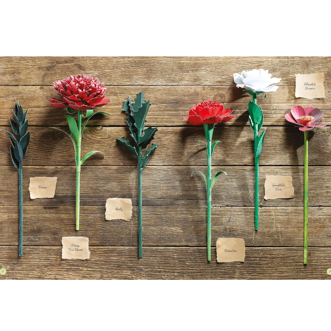 Six artificial flowers with handwritten paper labels are arranged on a rustic wooden background. The flowers include red, white, and pink blooms with green stems and leaves.