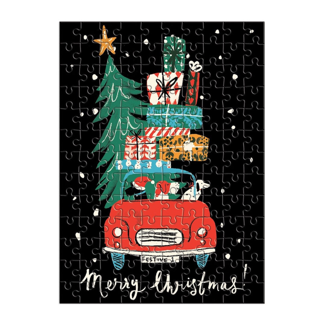 A completed jigsaw puzzle featuring a festive Christmas illustration: a red vintage car carrying a tall green Christmas tree and stacked gift boxes, on a black background with white snow-like specks and the words 'Merry Christmas!' at the bottom.