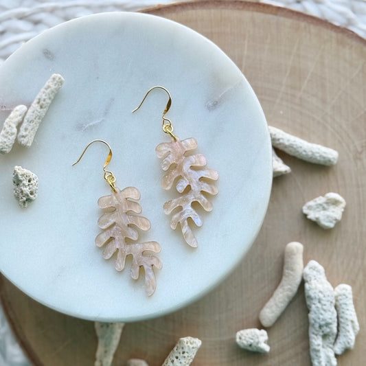 light pink Coral-shaped earrings on a marble surface with coral decorations.