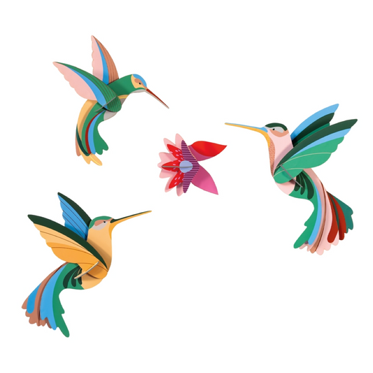 Three colorful 3D cardboard hummingbird cutout models and a flower piece arranged on a plain white background.