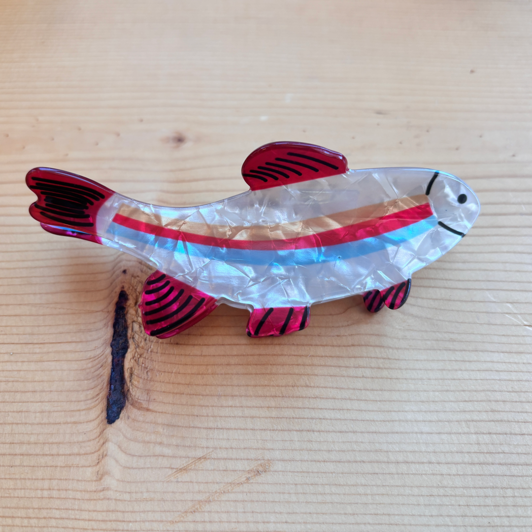 A fish shaped hair clip that has red, blue, and orange stripes down its center