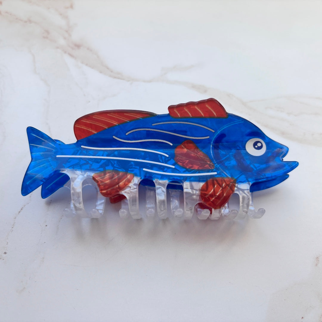 Blue fish-shaped hair clip with red and white accents on a light background