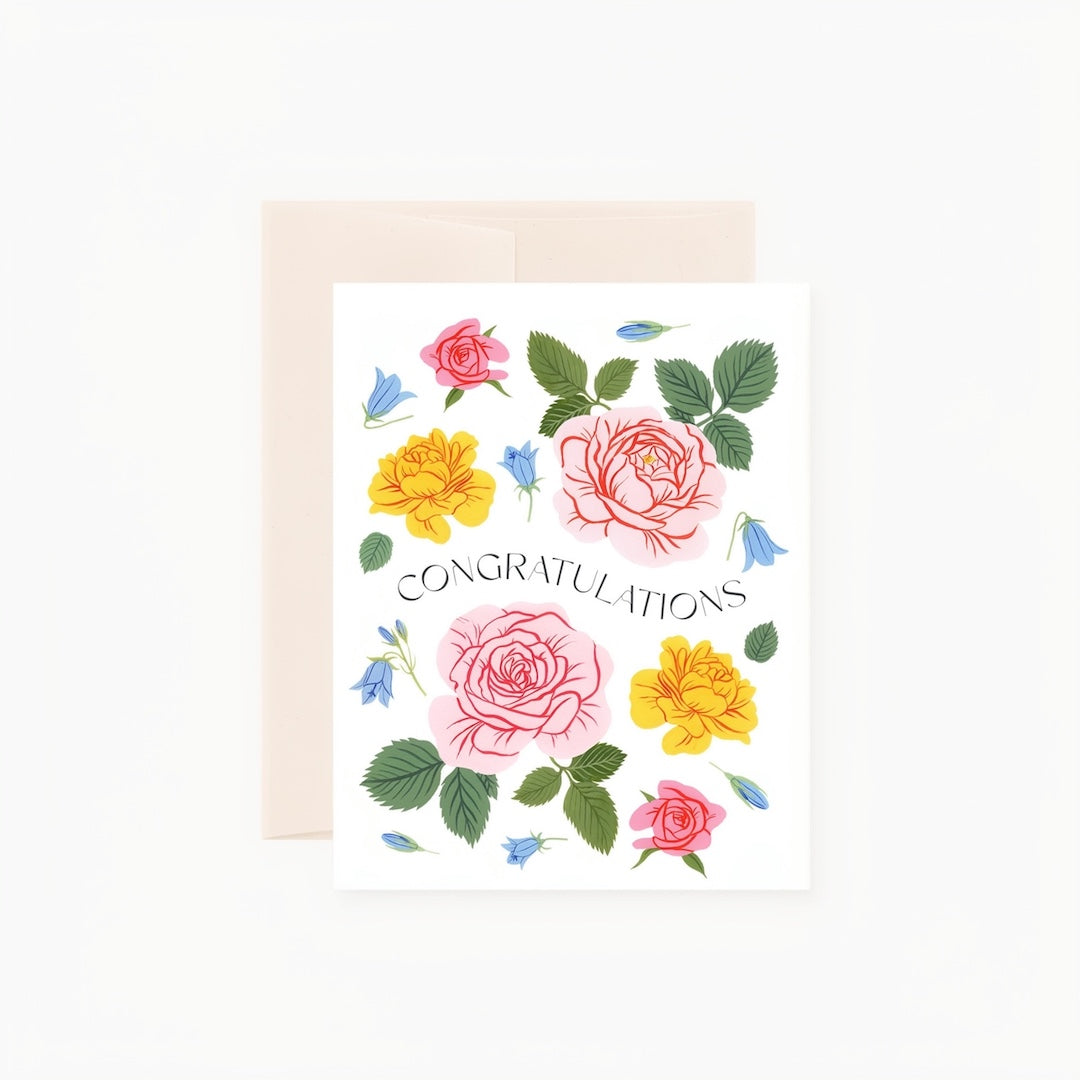 A white congratulations greeting card with a pastel floral illustration, shown with a light beige envelope behind it on a clean white background.