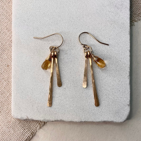 Pair of gold earrings with citrine stones on a textured surface