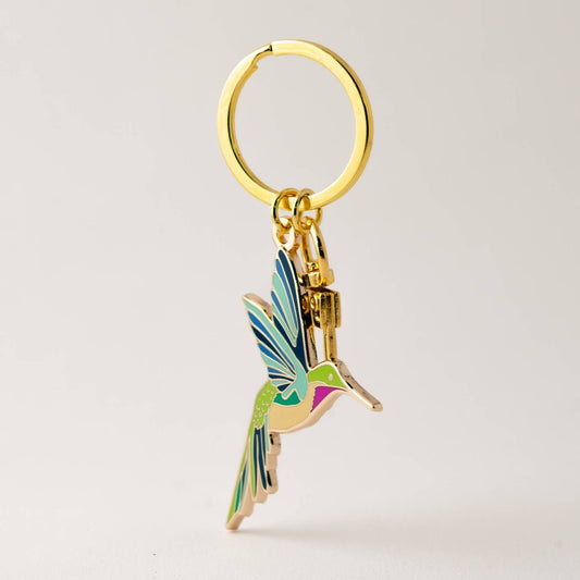 Gold keychain with a colorful hummingbird charm on a light gray background