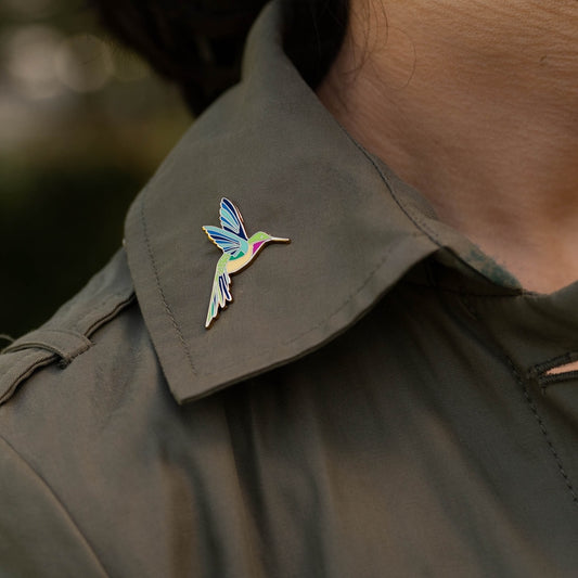 Hummingbird pin on a green jacket collar with a blurred natural background