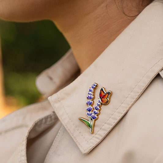Pin with lavender flower and butterfly on a beige jacket against a blurred natural background