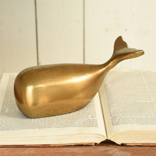 Gold whale-shaped object on an open book with a wooden surface and light background