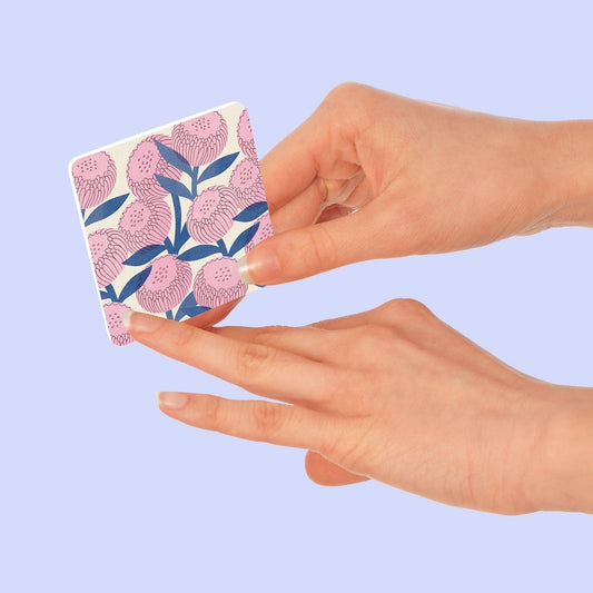 Hand holding a square nail file with floral design against a light purple background