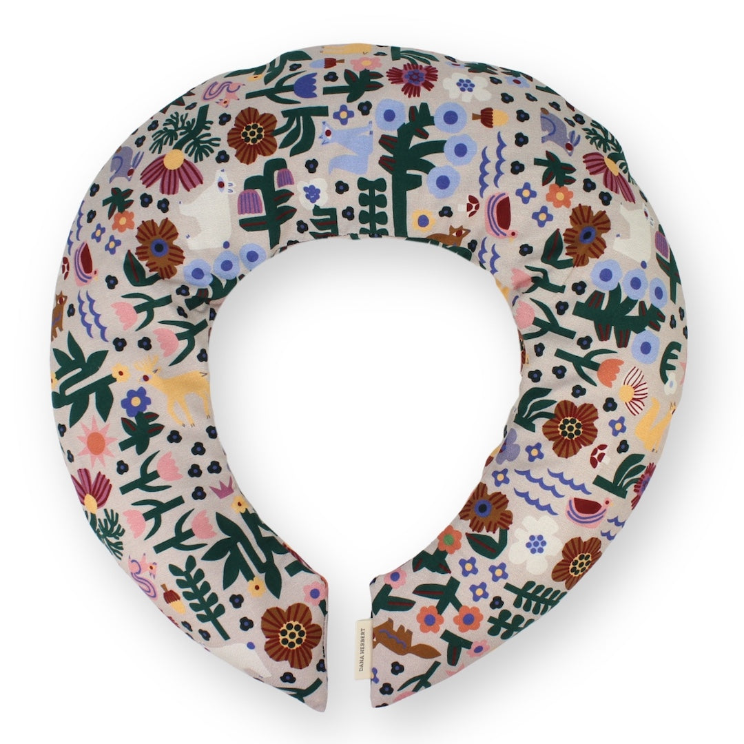A padded neck pillow with a dense, colorful folk-art floral and botanical pattern on a cream background, shown against a plain white background.