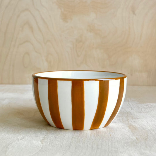 Ceramic bowl with ochre and white stripes on a light wooden surface