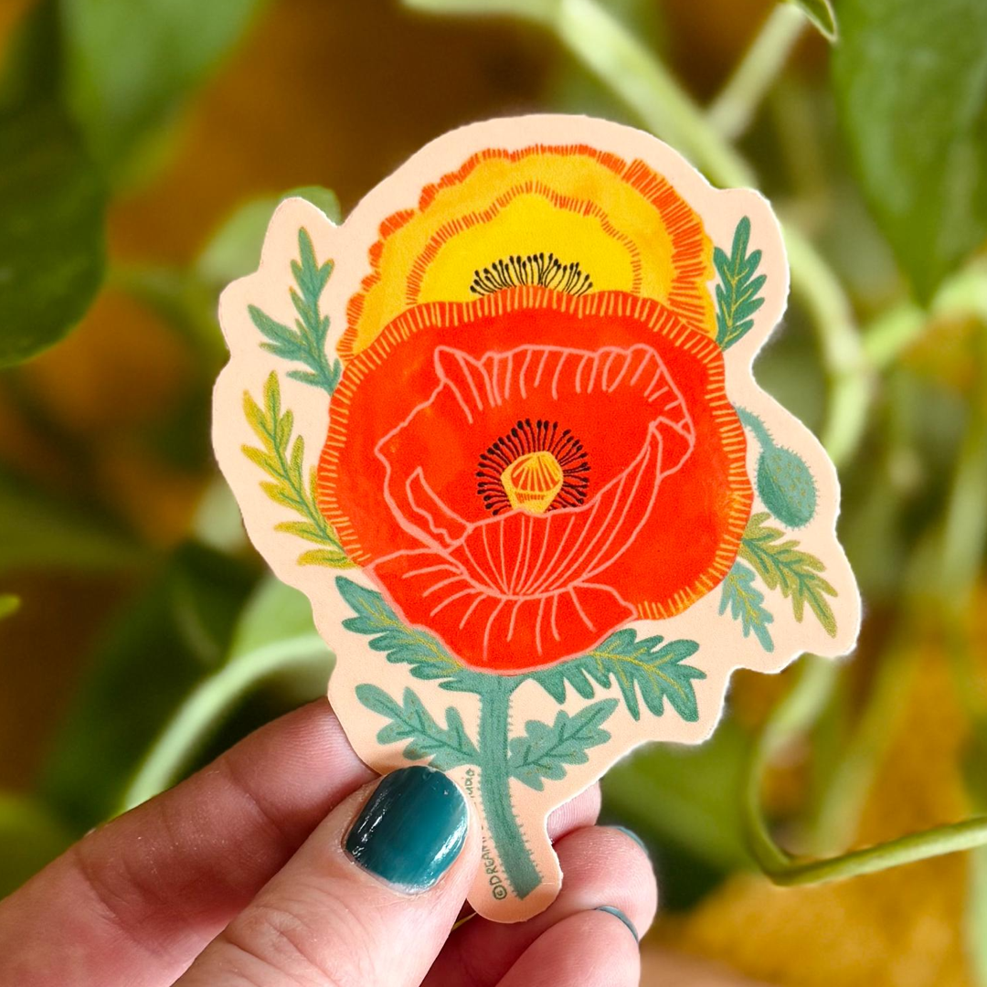 Hand holding a colorful poppy sticker with green leaves against a blurred natural background