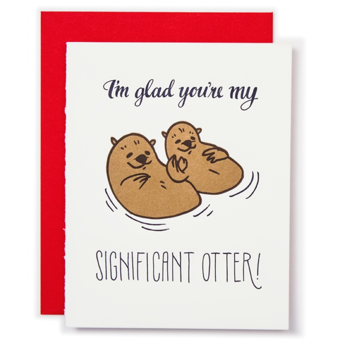 A white greeting card with a red envelope behind it, featuring a cute illustration of two brown otters floating in water and the text 'I'm glad you're my SIGNIFICANT OTTER!'.