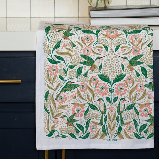 Decorative towel with floral and hummingbird pattern hanging on a cabinet.