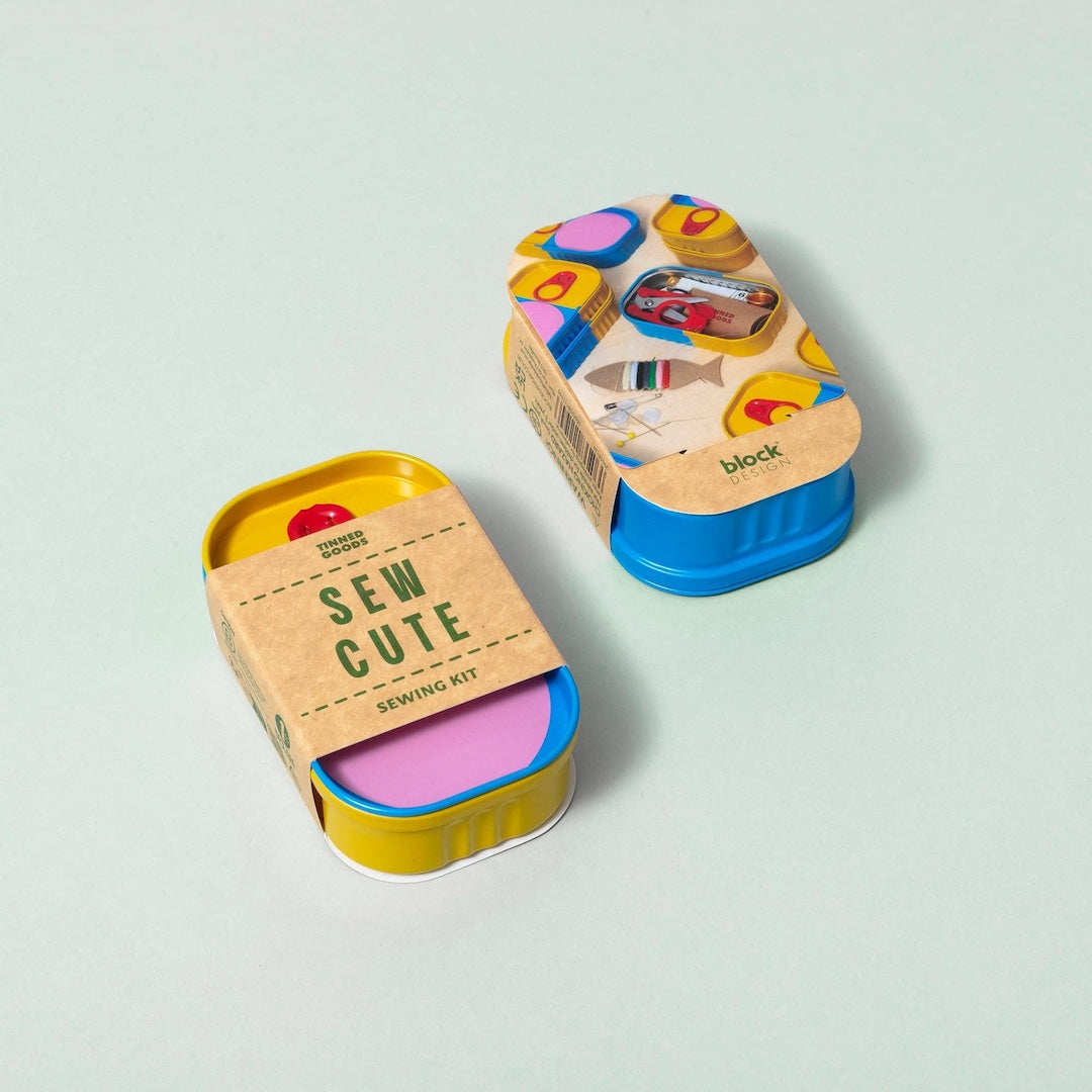 A sewing kit in a small metal tin with a kraft paper label reading 'SEW CUTE SEWING KIT' on the front, shown open with colorful thread spools and accessories inside. A second view of the closed tin with printed packaging sits behind it on a pale mint background.