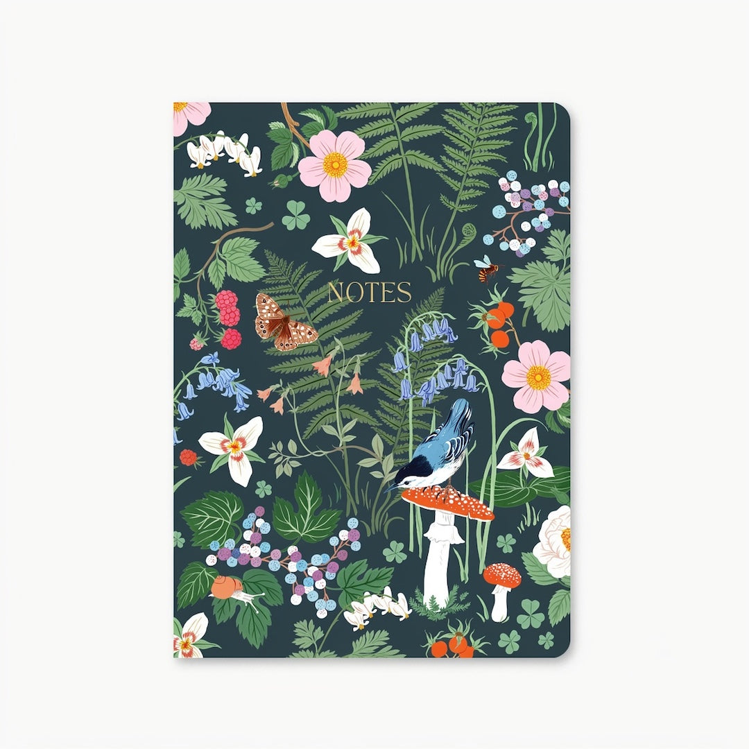 Notebook with a dark cover and a woodland inspired pattern that features a bird, moth, mushrooms, flowers, and fern leaves. In the center of the cover "Notes" is written in gold. Shown on a white background.