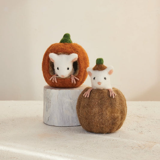 Two felted wool mouse figurines peeking from pumpkins, displayed on a light surface against a soft beige background.