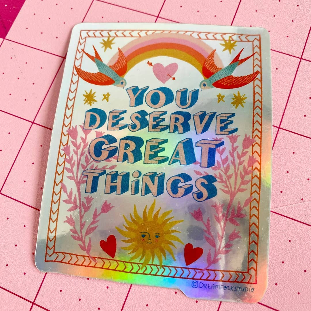 Holographic sticker with motivational text 'You deserve great things' on a pink grid background