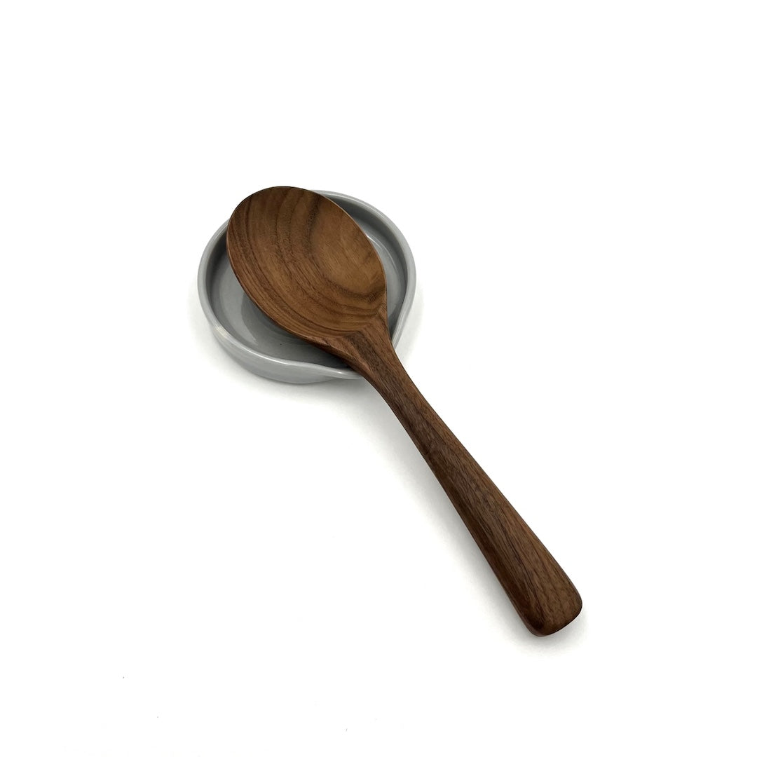 A dark brown wooden spoon resting on a small round gray ceramic dish, set against a plain white background.
