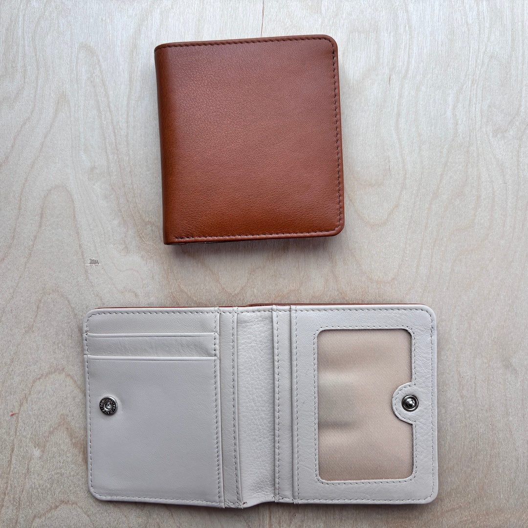 A brown leather bifold wallet shown closed above an open matching wallet displaying its interior compartments, card slots, and ID window on a light wood background.