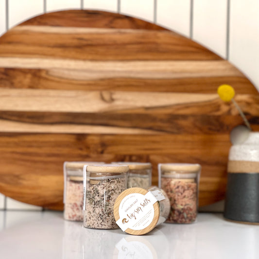 Wooden cutting board with glass containers of salts on a white surface