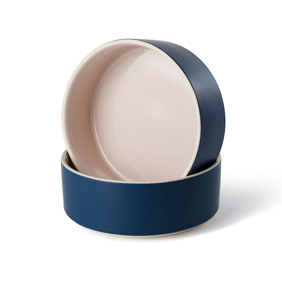 Two ceramic bowls with navy exteriors and beige interiors on a white background