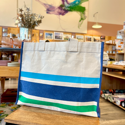 Blue and green striped tote on wooden side table with large painting in background.