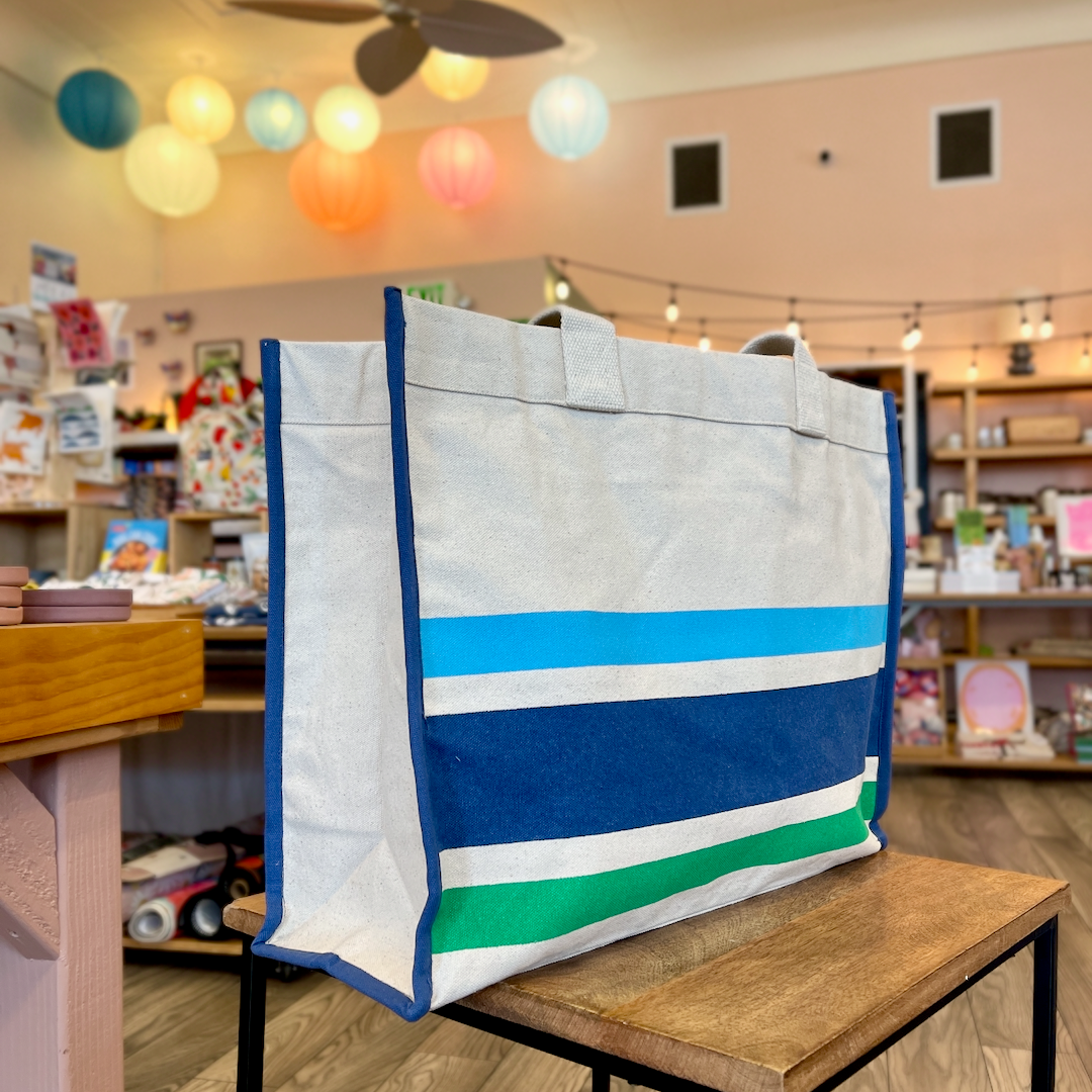 Blue and green striped tote on wooden side table with colorful paper lanterns in background.