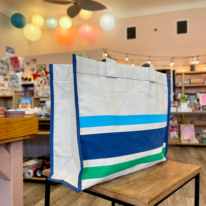 Blue and green striped tote on wooden side table with colorful paper lanterns in background.