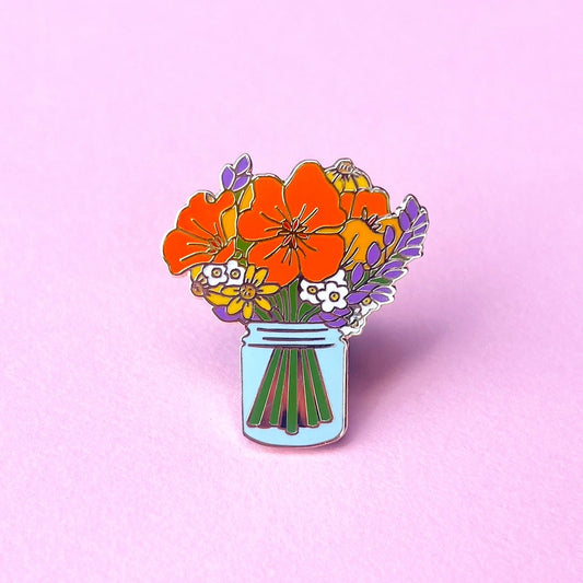 Floral design pin with orange poppies, lavender sprigs, and yellow flowers in a blue jar on a pink background