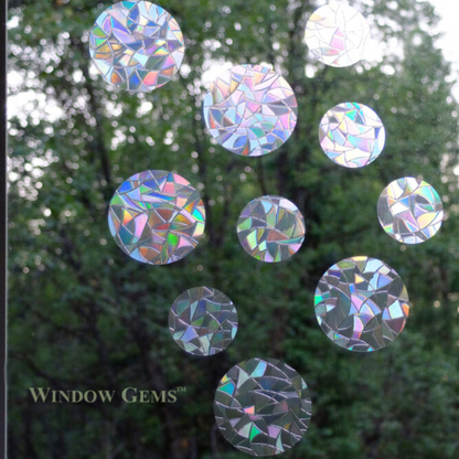 Circular iridescent window stickers on a window with a blurred green outdoor background