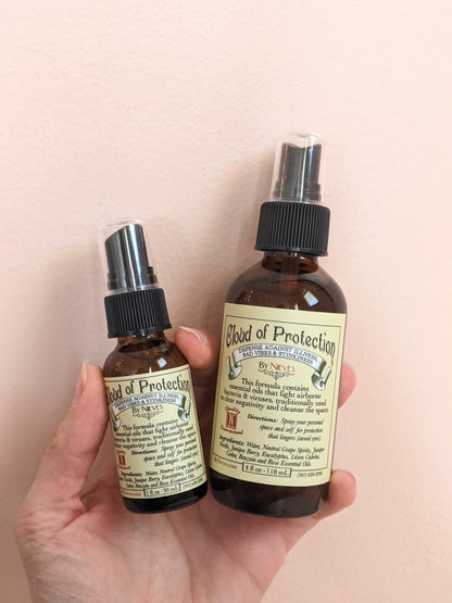 Two bottles labeled 'Cloud of Protection' held in a hand against a beige background