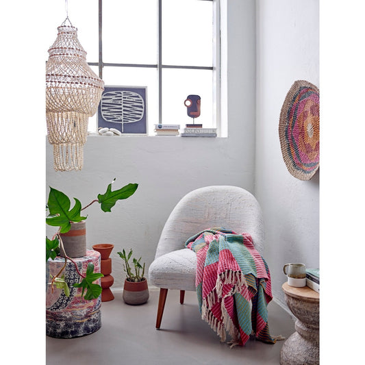 Cozy corner with a chair draped with a colorful blanket, plants, and decorative items.