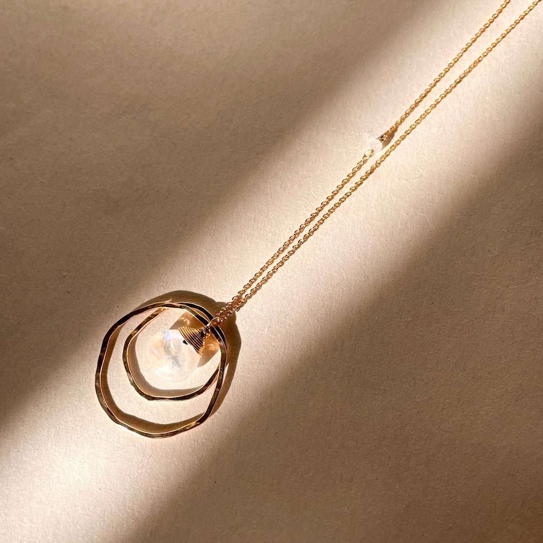 Gold necklace with 2 open circles and a moonstone in the center on a beige background