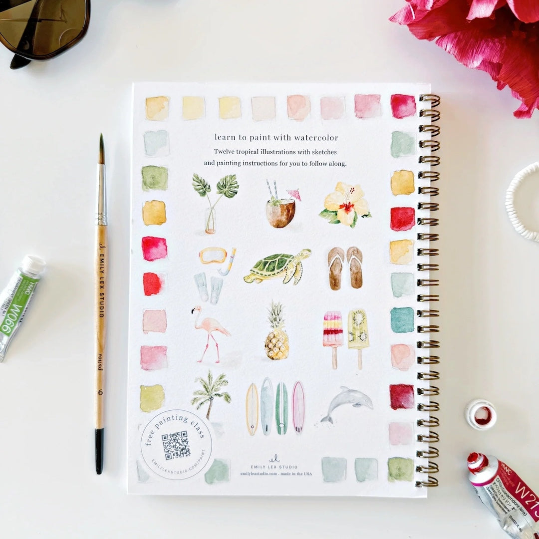Artistic coloring book with watercolor illustrations on a white surface with art supplies.
