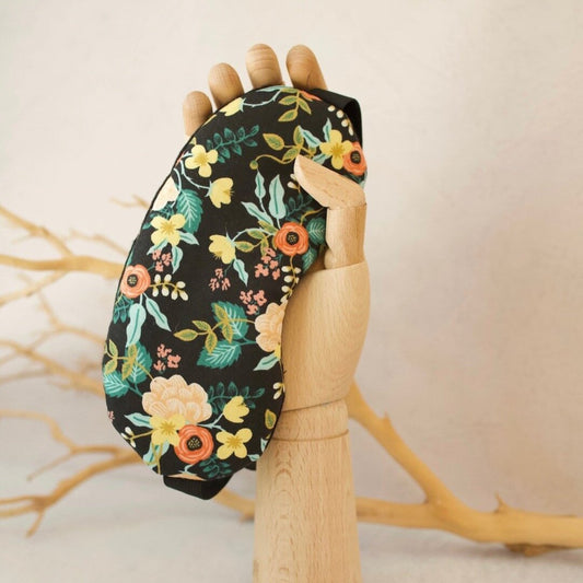 Floral-patterned eye mask held on a wooden mannequin arm against a neutral background