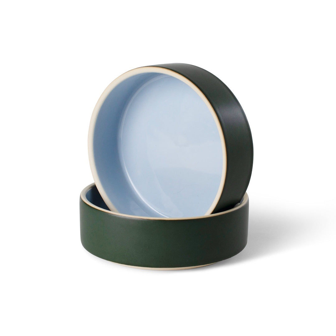 Two ceramic bowls with dark green exteriors stacked on a white background