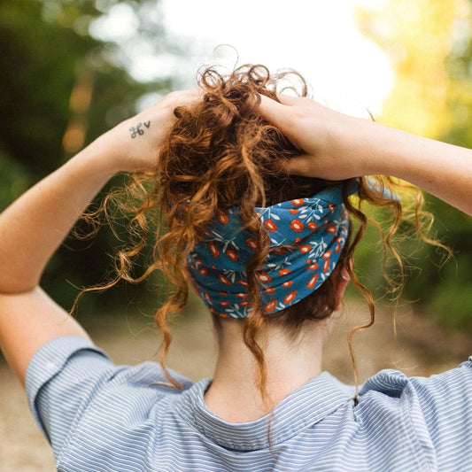 Person with curly hair wearing a blue bandana with orange patterns, standing outdoors.