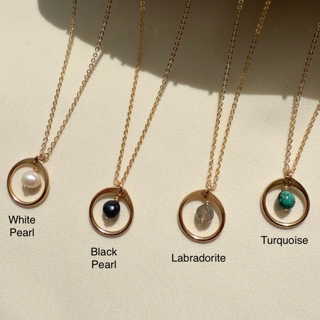 Four gold necklaces with different gemstones on a beige background