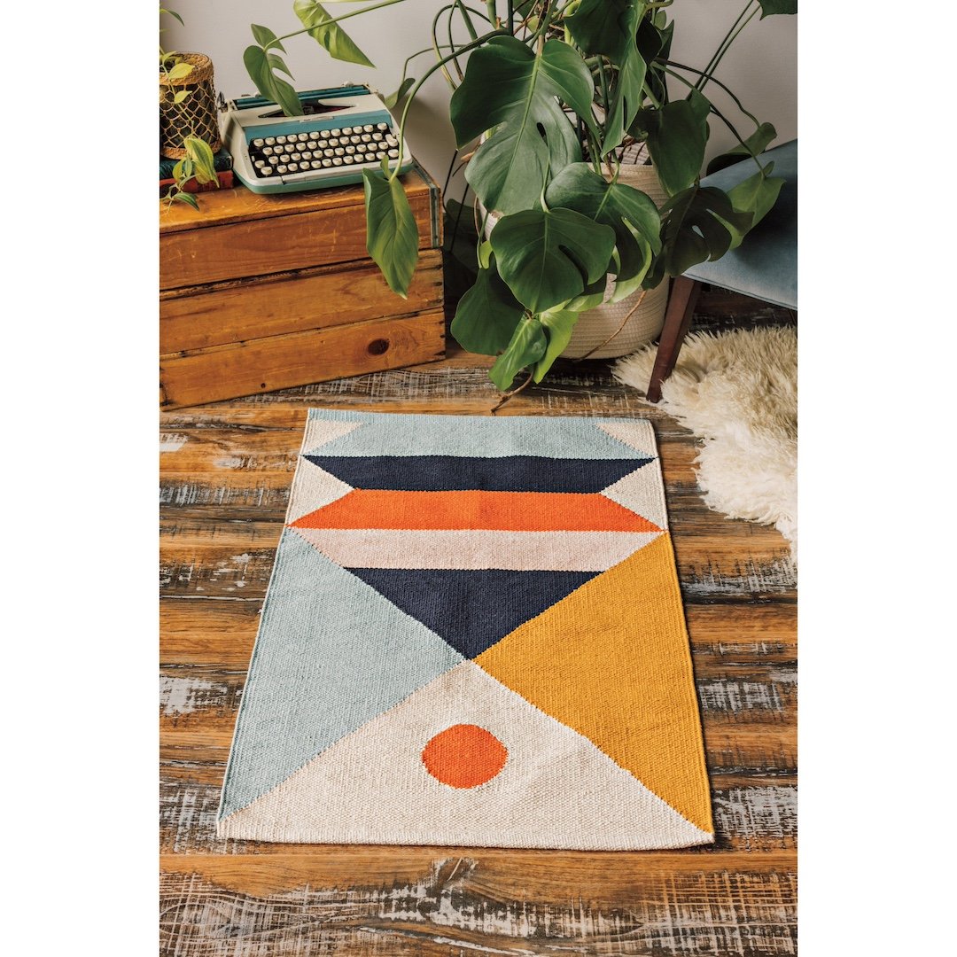 Geometric patterned rug on a wooden floor with plants and a typewriter in the background