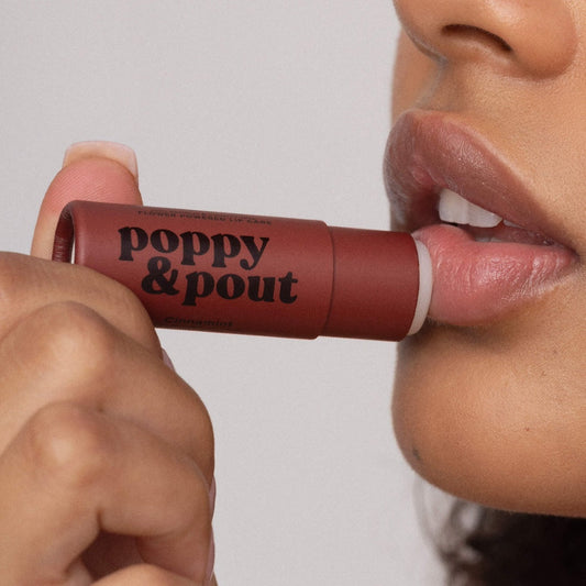 Person applying a lip balm labeled 'poppy & pout' to their lips.
