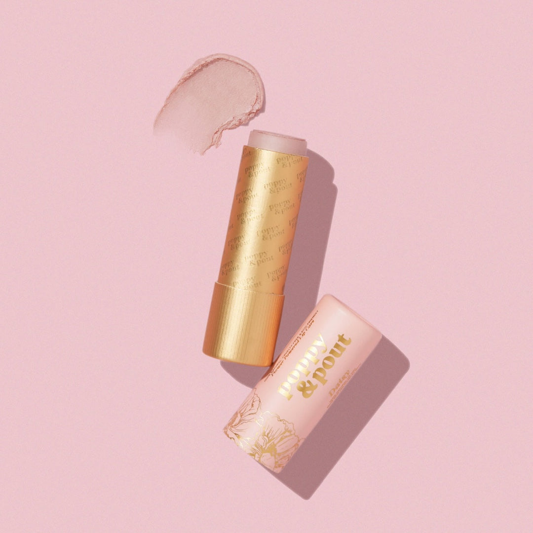 Poppy & Pout Daisy lip tint in a gold tube on a pink background
