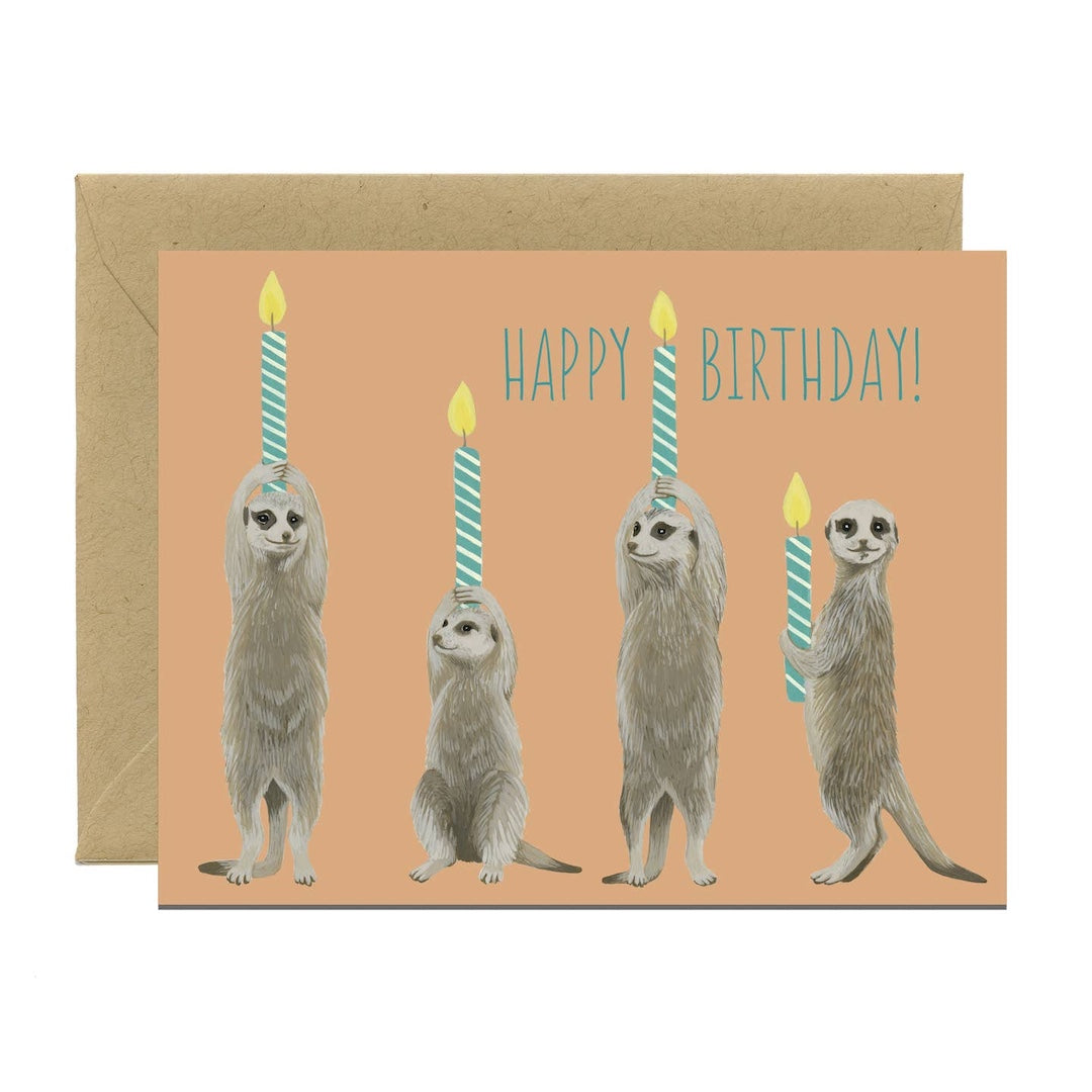 Birthday card with meerkats holding candles and 'Happy Birthday!' text on a peach background.
